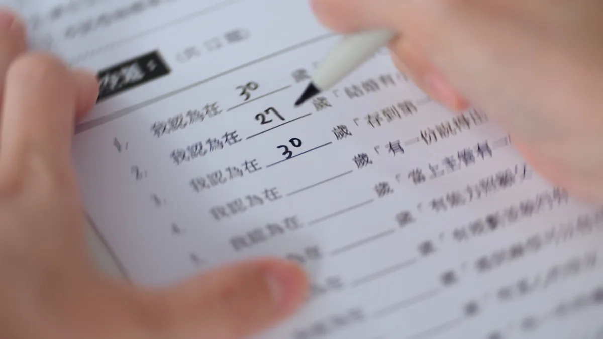 手握著筆填寫問卷的特寫，紙上寫著「我認為在 30 歲」